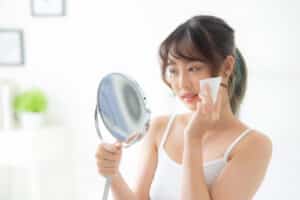 asian woman smile with skin care use oil blotting paper on face looking mirror