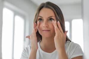 Woman gently touching the skin beneath her eyes while considering treatment for under-eye bags and puffiness.