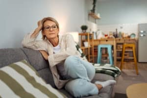 Woman sitting thoughtfully on a sofa at home, representing concerns about urinary incontinence.