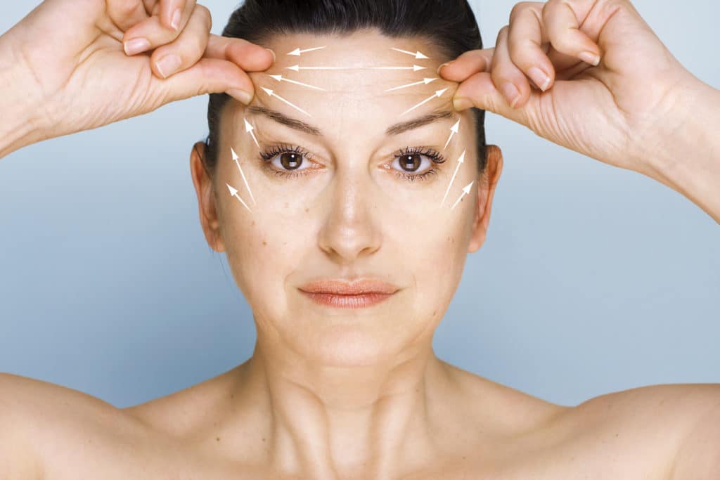 Portrait of 50 year old woman looking at camera, lifting her forehead wrinkles with guidelines showing lifting direction