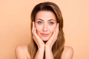Middle-aged woman holds her hands to her face, pleased with their rejuvenated appearance.
