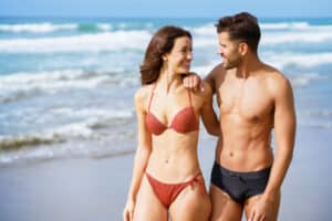 A fit couple with defined abdominal muscles walks along the beach