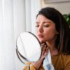 Woman looks at scarring in the mirror after acne outbreak.