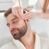 Why More Men Are Choosing Non-Surgical Cosmetic Treatments Man in robe gets a facial from a cosmetic dermatologist for improved skin texture.