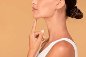 Woman’s side profile, as she points to her well-defined chin from chin contouring with dermal fillers.